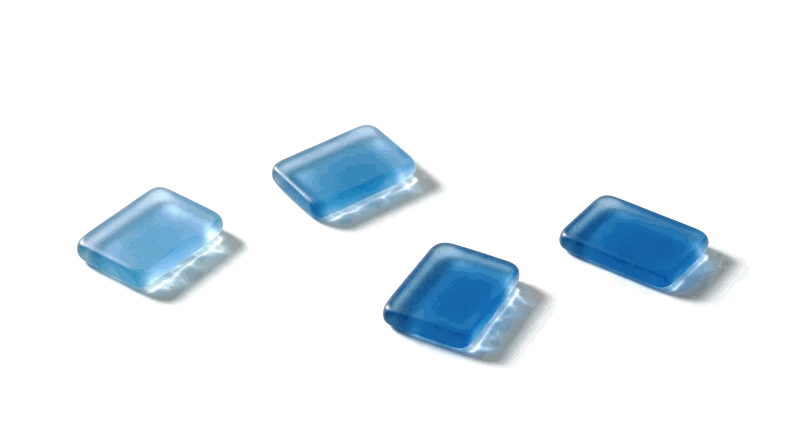 Four frosted blue glass tiles lying far apart on a white studio ground